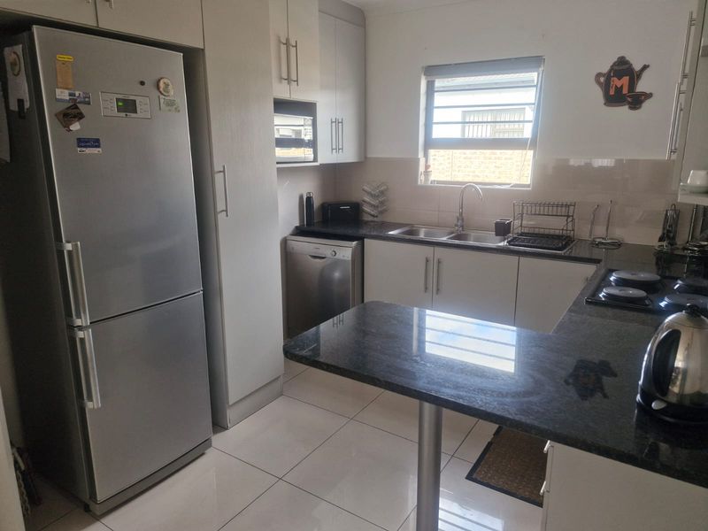 A functional kitchen featuring granite countertops, ample built-in cabinetry, a stainless steel sink, and a built-in hob with tiled flooring.