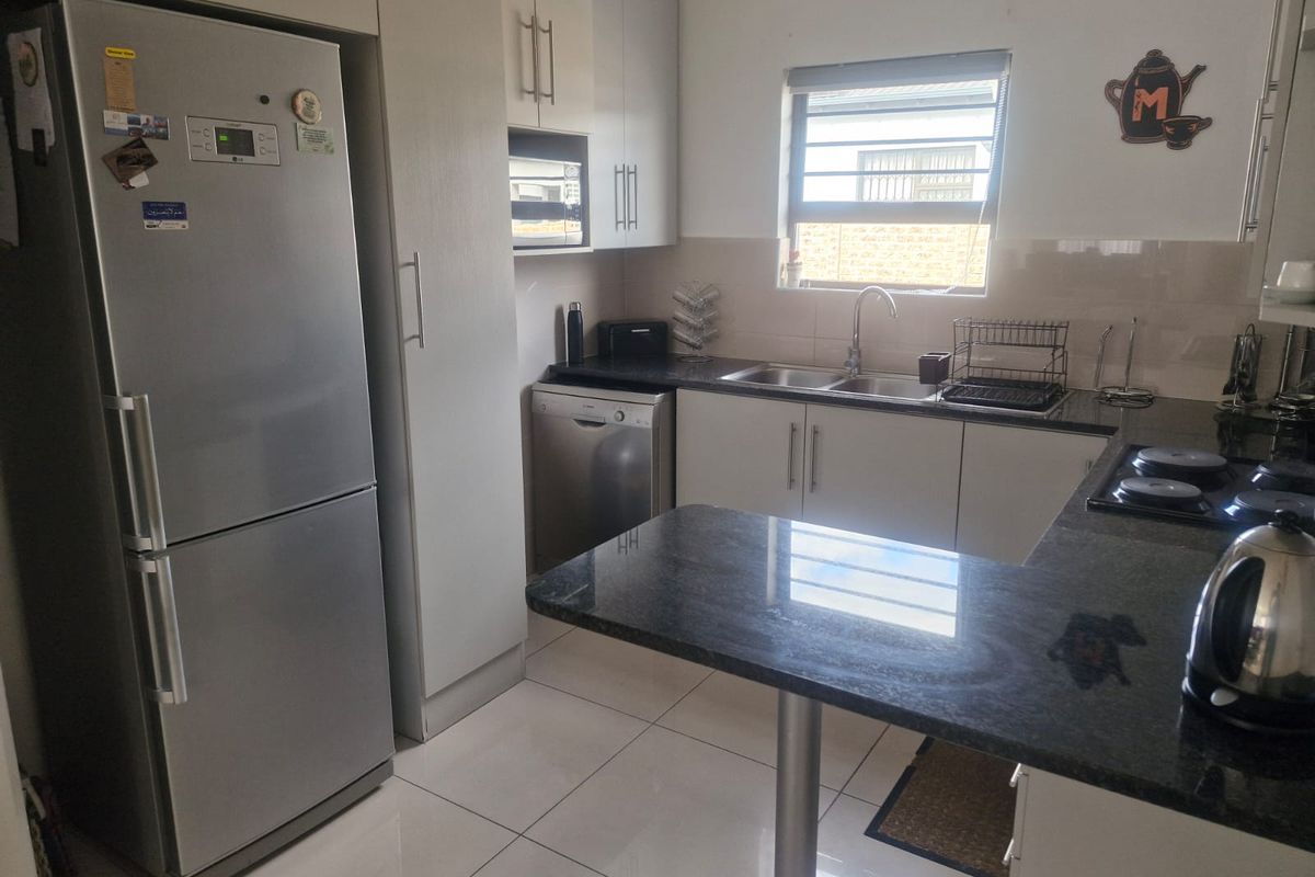 A functional kitchen featuring granite countertops, ample built-in cabinetry, a stainless steel sink, and a built-in hob with tiled flooring.