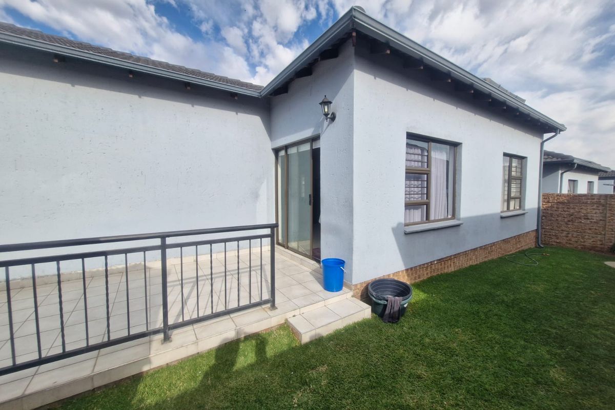 Rear view of the townhouse featuring a tiled patio with metal railing, sliding door access, and a well-maintained garden area.