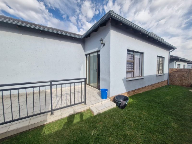 Rear view of the townhouse featuring a tiled patio with metal railing, sliding door access, and a well-maintained garden area.