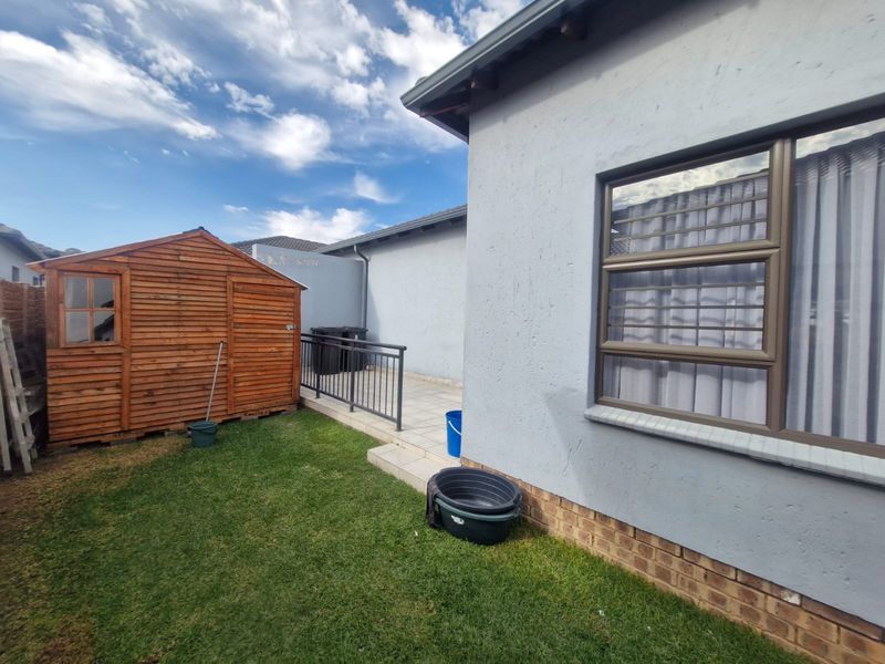 Rear exterior view of the townhouse featuring a small lawn, a timber garden shed, and a paved patio area with metal railing.