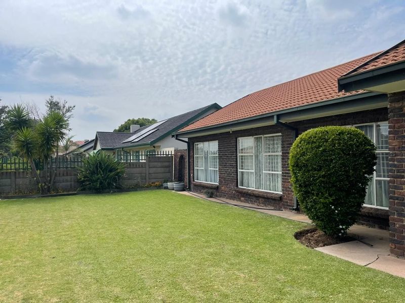 A well-maintained rear exterior view of a brick house featuring a tiled roof, aluminum windows, and a spacious lawn with boundary walling.