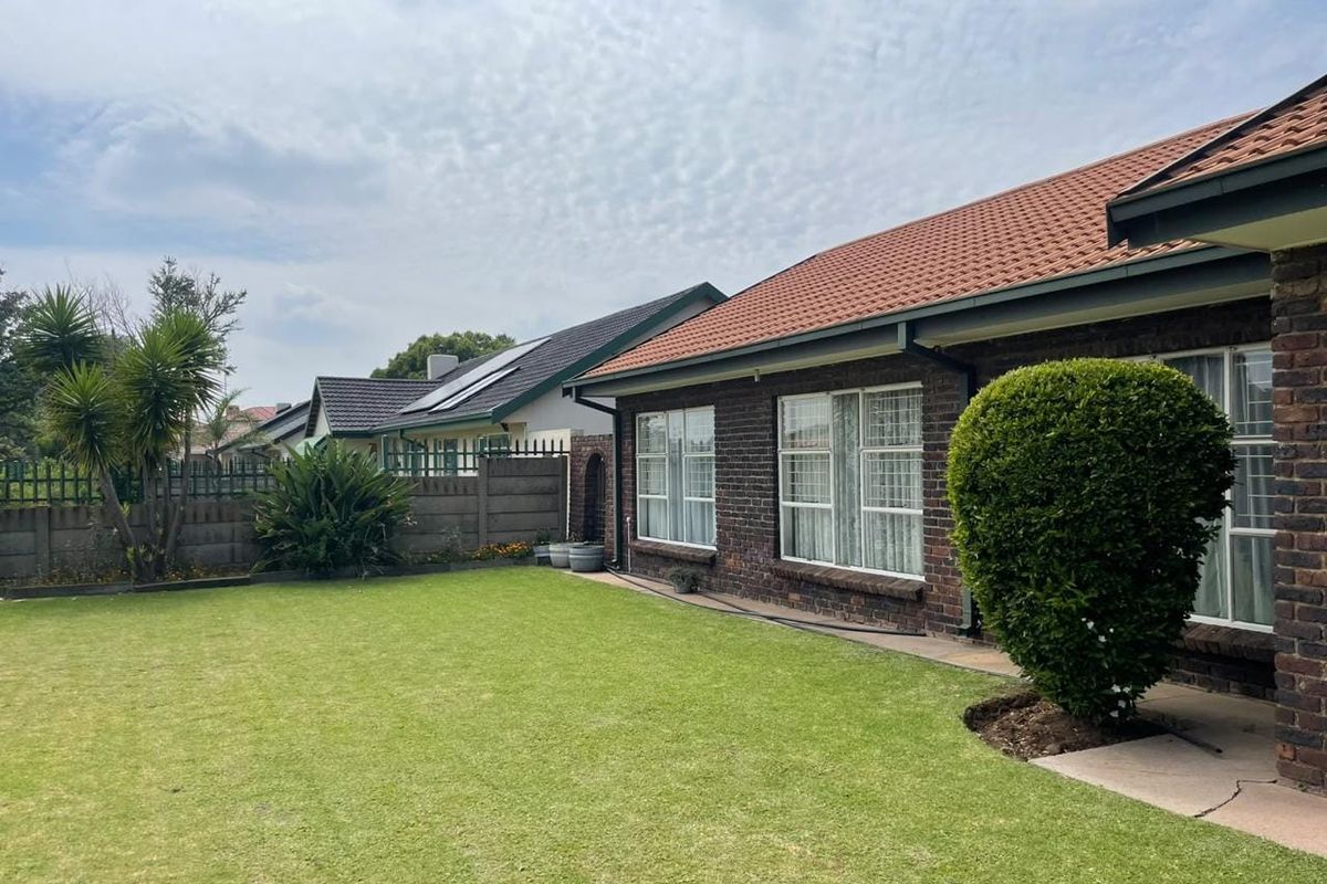 A well-maintained rear exterior view of a brick house featuring a tiled roof, aluminum windows, and a spacious lawn with boundary walling.