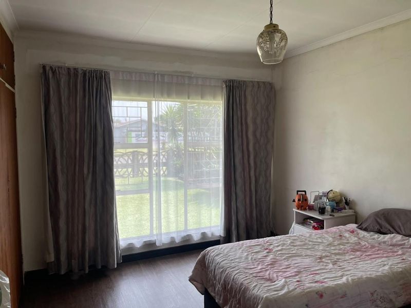 A bedroom featuring laminate flooring, a pendant light, and a large window with security bars, offering natural light and garden views.