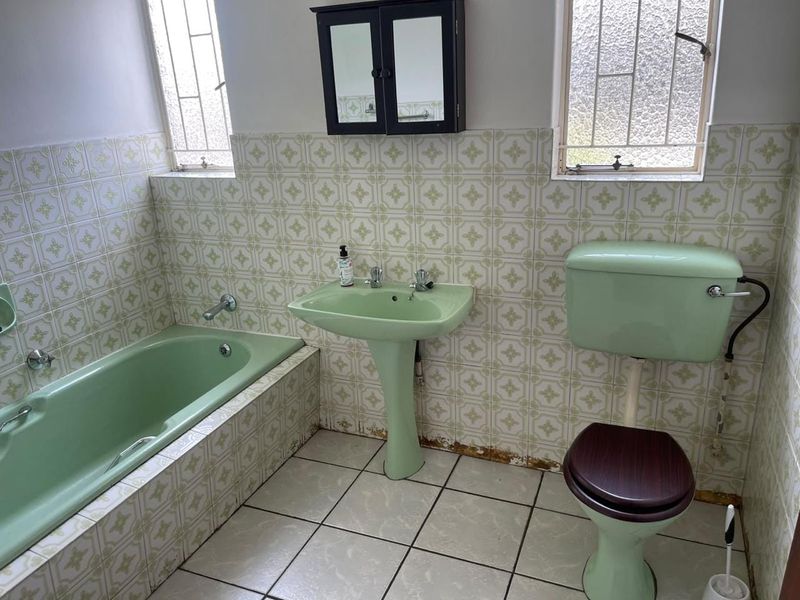A dated bathroom featuring original green sanitaryware, tiled walls and flooring, and security bars on the windows. Ideal for a modern renovation.