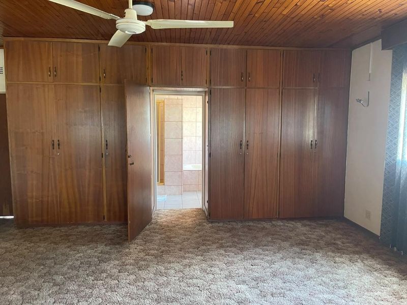 Spacious bedroom featuring extensive built-in wooden cabinetry, a timber-paneled ceiling with a ceiling fan, and direct access to an en-suite bathroom.