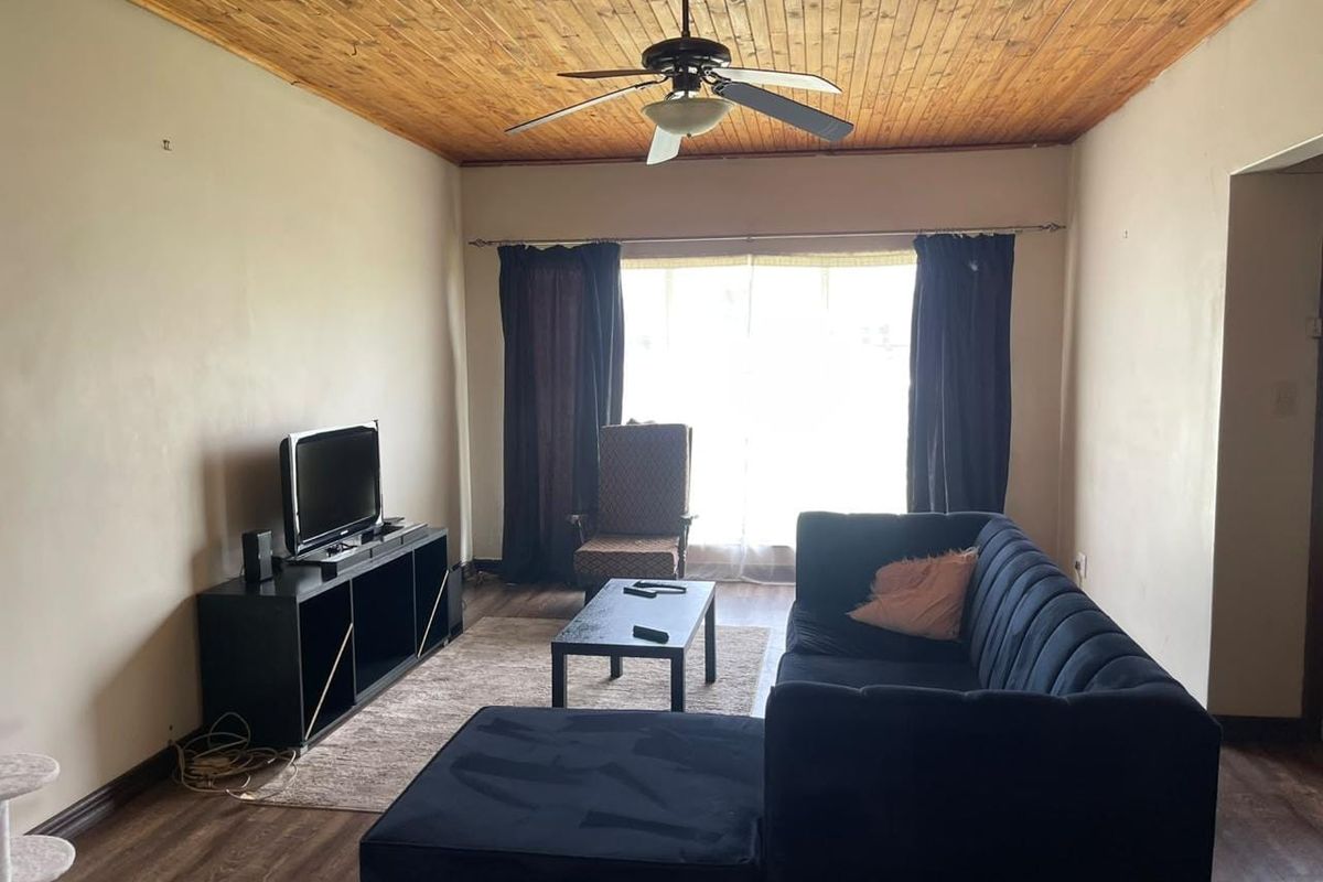 A living room featuring a timber-clad ceiling with a central ceiling fan and laminate flooring, providing a neutral base for interior updates.