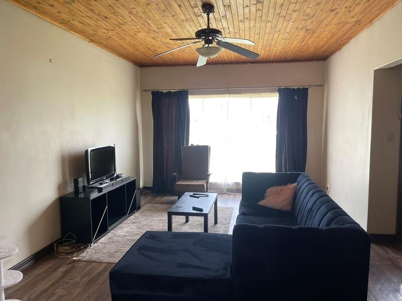 A living room featuring a timber-clad ceiling with a central ceiling fan and laminate flooring, providing a neutral base for interior updates.
