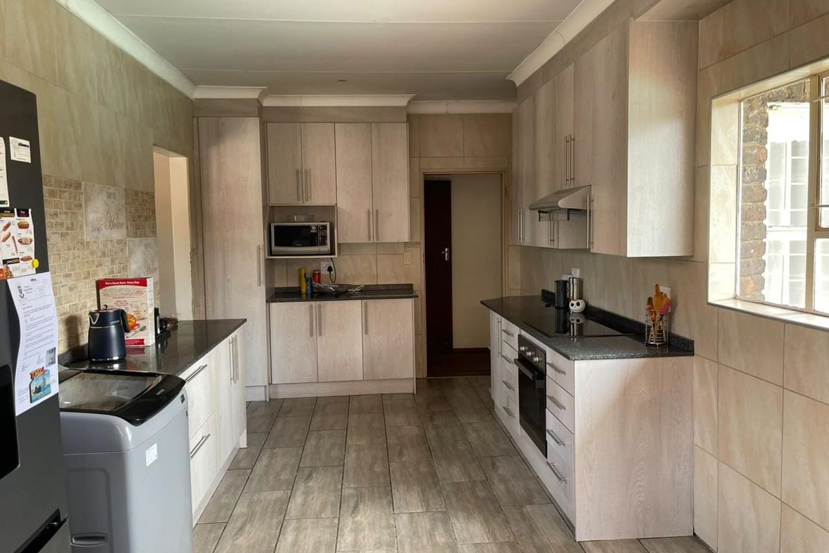 A functional kitchen featuring light wood-finish cabinetry, granite countertops, built-in appliances, and neutral tiled flooring and wall finishes.