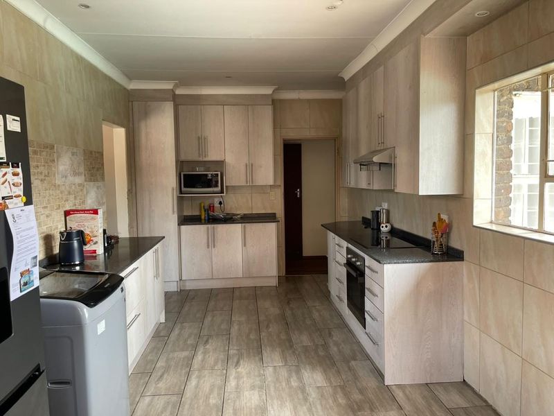 A functional kitchen featuring light wood-finish cabinetry, granite countertops, built-in appliances, and neutral tiled flooring and wall finishes.