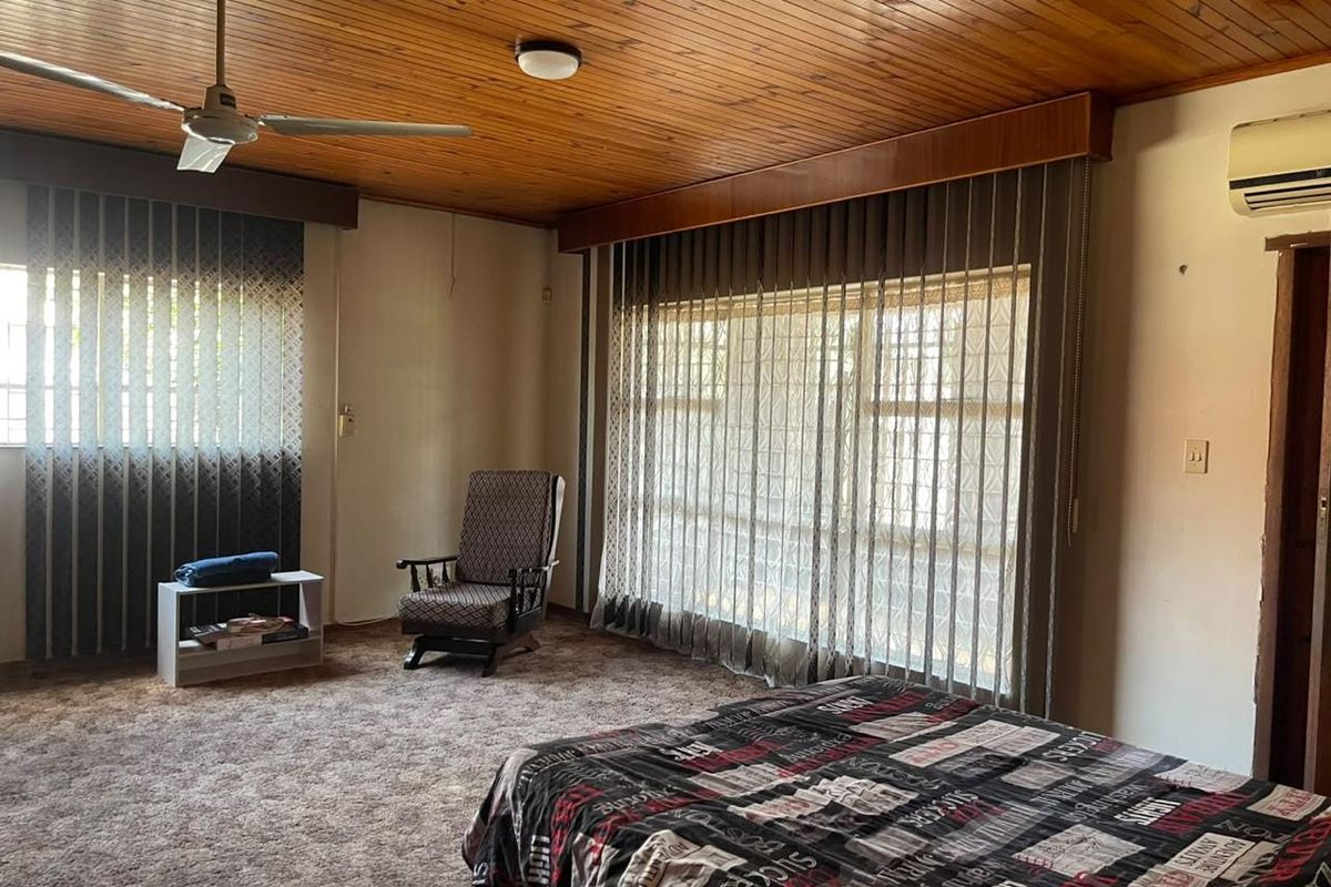 Spacious bedroom featuring a timber-clad ceiling, wall-mounted air conditioning, and carpeted flooring, offering a dated aesthetic ready for modernization.