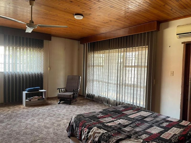 Spacious bedroom featuring a timber-clad ceiling, wall-mounted air conditioning, and carpeted flooring, offering a dated aesthetic ready for modernization.