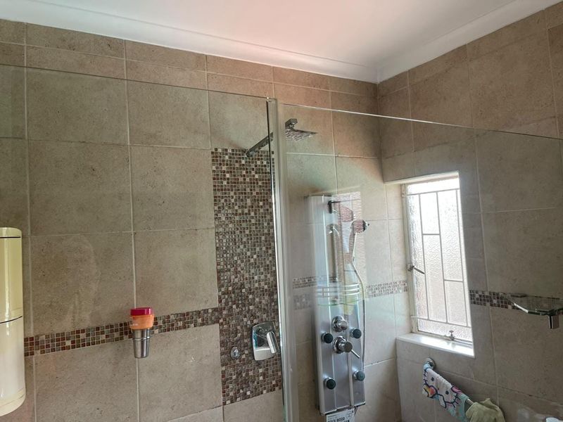 A bathroom featuring a glass-enclosed shower with a modern shower panel system, mosaic tile accents, and neutral wall tiling.