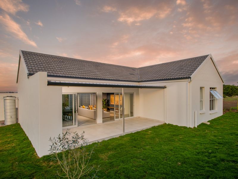 Rear view of a modern residential property featuring a covered patio, sliding glass doors, and a well-maintained lawn at sunset.