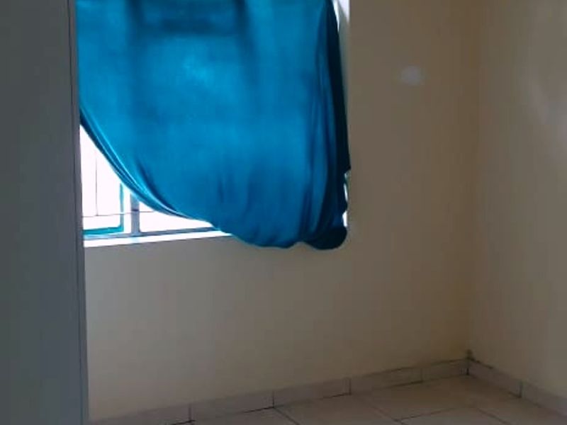 A vacant bedroom featuring tiled flooring, a built-in cupboard, and a window with security bars, requiring minor cosmetic updates to the wall finishes.
