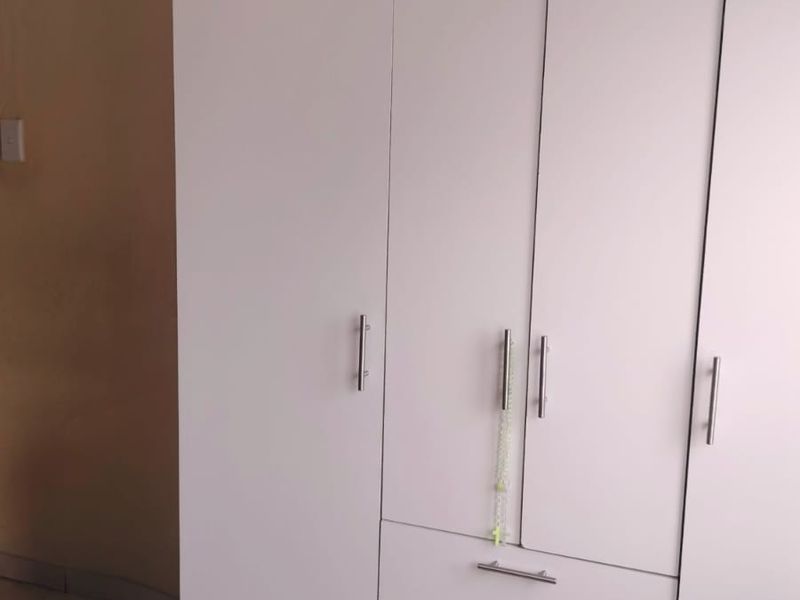 A bedroom featuring a white built-in wardrobe with integrated drawers and tiled flooring.