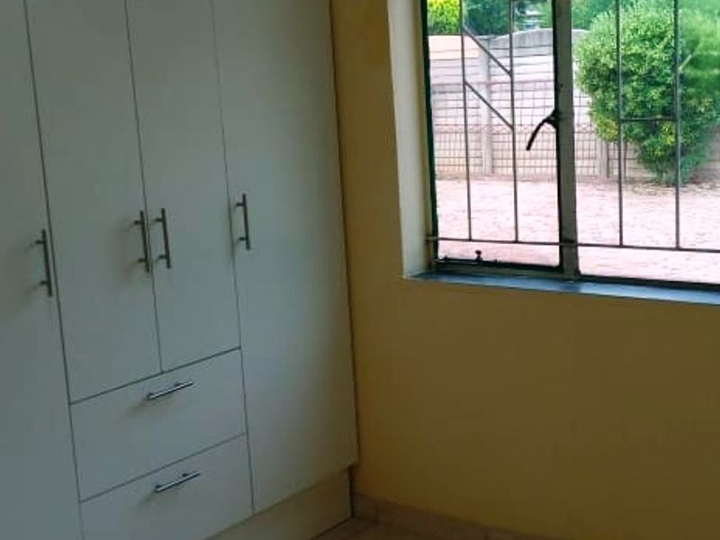 A compact bedroom featuring built-in wardrobes, tiled flooring, and security bars on the window, offering a functional space ready for personalization.