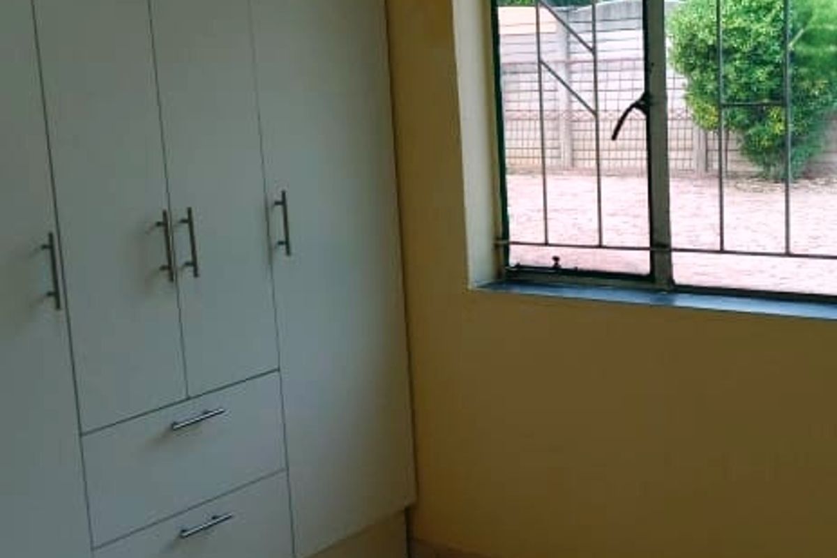 A compact bedroom featuring built-in wardrobes, tiled flooring, and security bars on the window, offering a functional space ready for personalization.