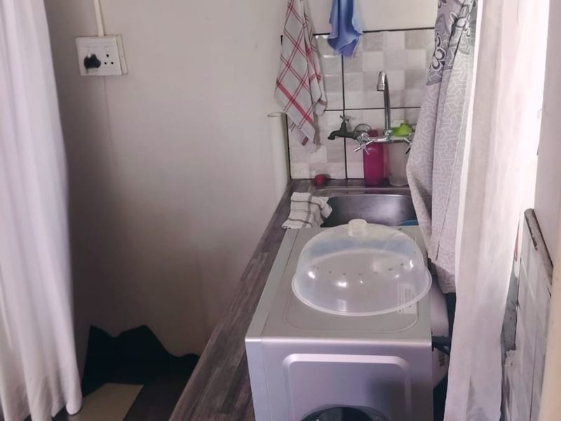 A compact scullery or kitchenette area featuring a stainless steel sink, laminate countertop, and tiled splashback.