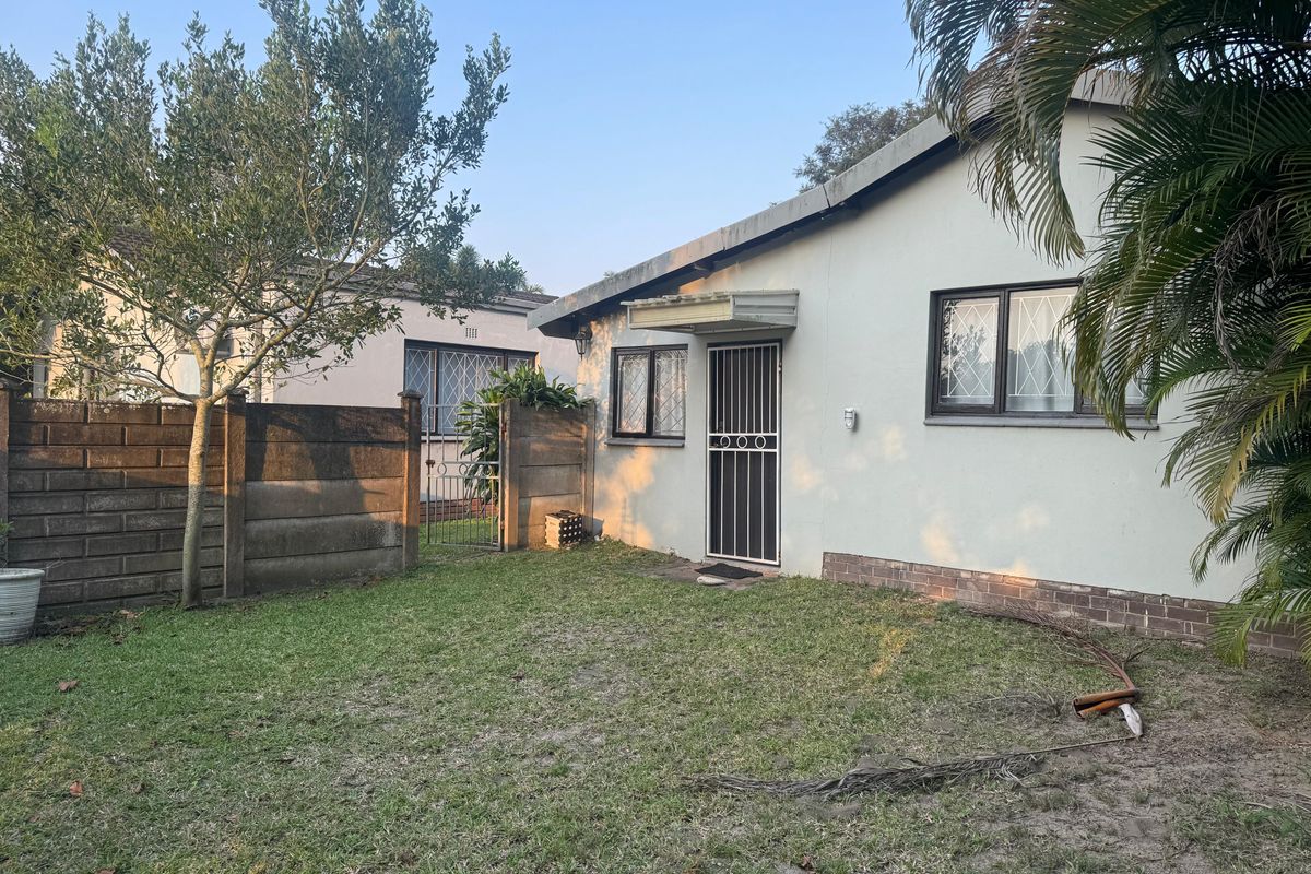 Rear view of the property featuring a lawn, precast concrete boundary wall, and a secure entrance with security gate and bars.