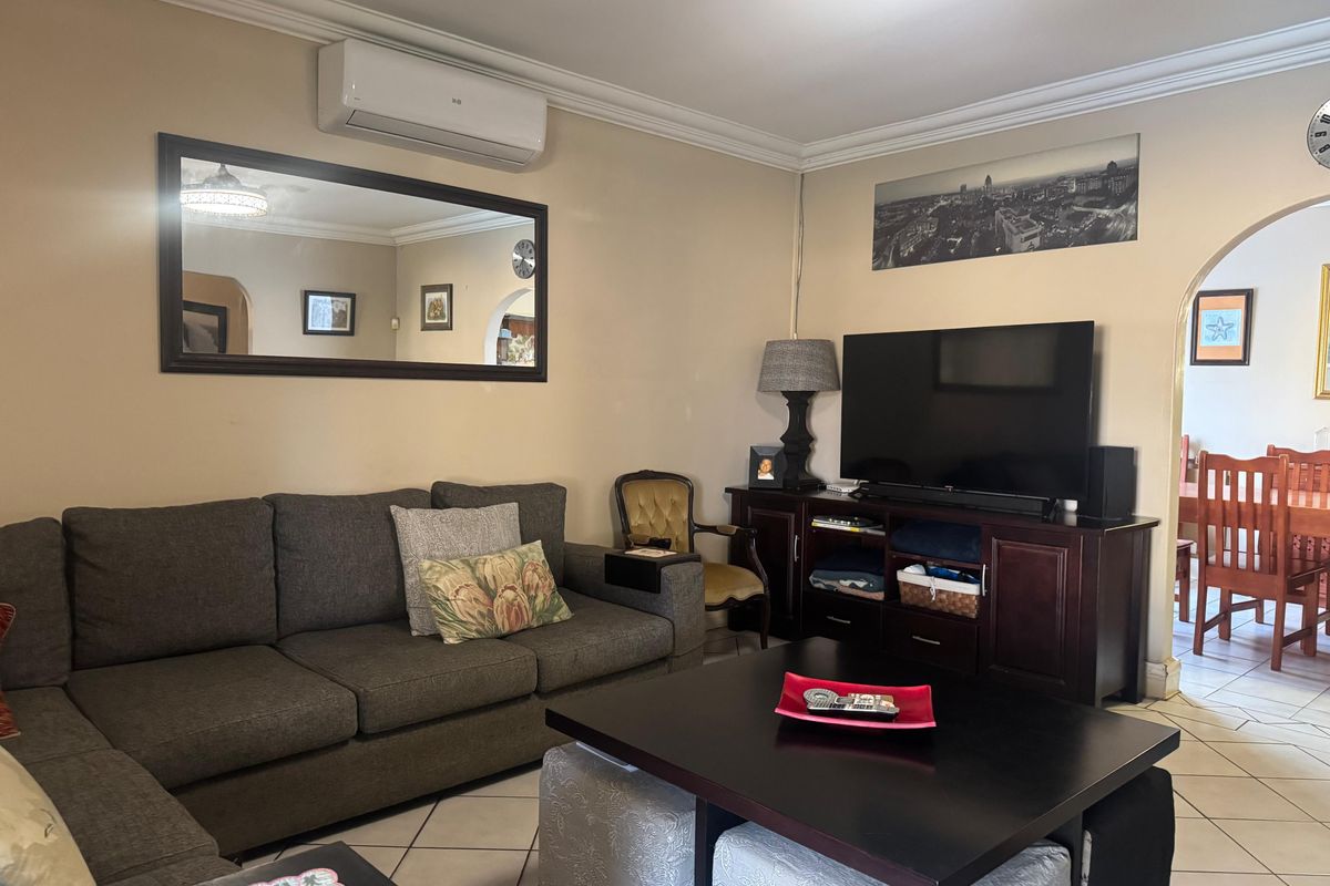 A comfortable living room featuring ceramic floor tiles, decorative cove cornicing, and a wall-mounted split-system air conditioner, with an arched doorway leading to the dining area.