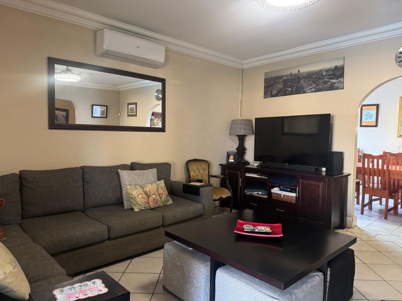 A comfortable living room featuring ceramic floor tiles, decorative cove cornicing, and a wall-mounted split-system air conditioner, with an arched doorway leading to the dining area.