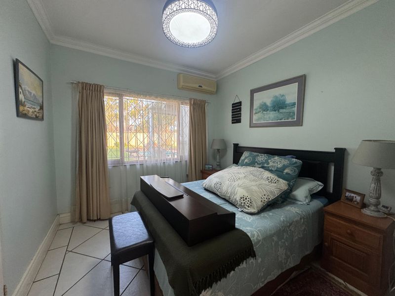A bedroom featuring tiled flooring, crown molding, a wall-mounted split-system air conditioner, and a window fitted with a security gate.