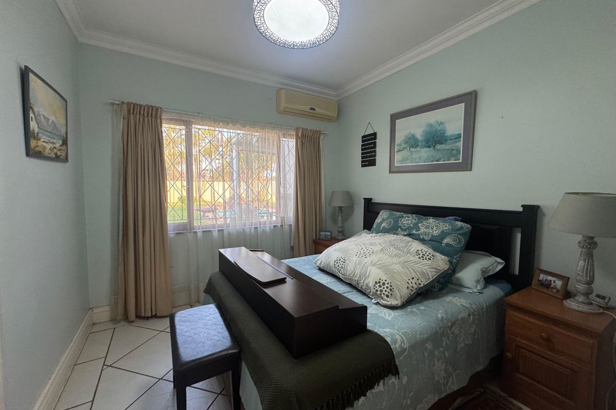 A bedroom featuring tiled flooring, crown molding, a wall-mounted split-system air conditioner, and a window fitted with a security gate.