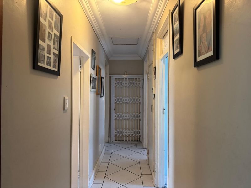A functional interior hallway featuring tiled flooring, decorative ceiling cornicing, and a secure metal gate at the end of the passage.