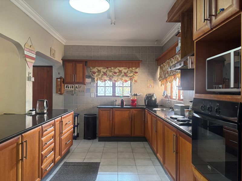 A functional kitchen featuring warm wooden cabinetry, granite countertops, built-in oven, hob, and tiled finishes, offering a classic and practical workspace.