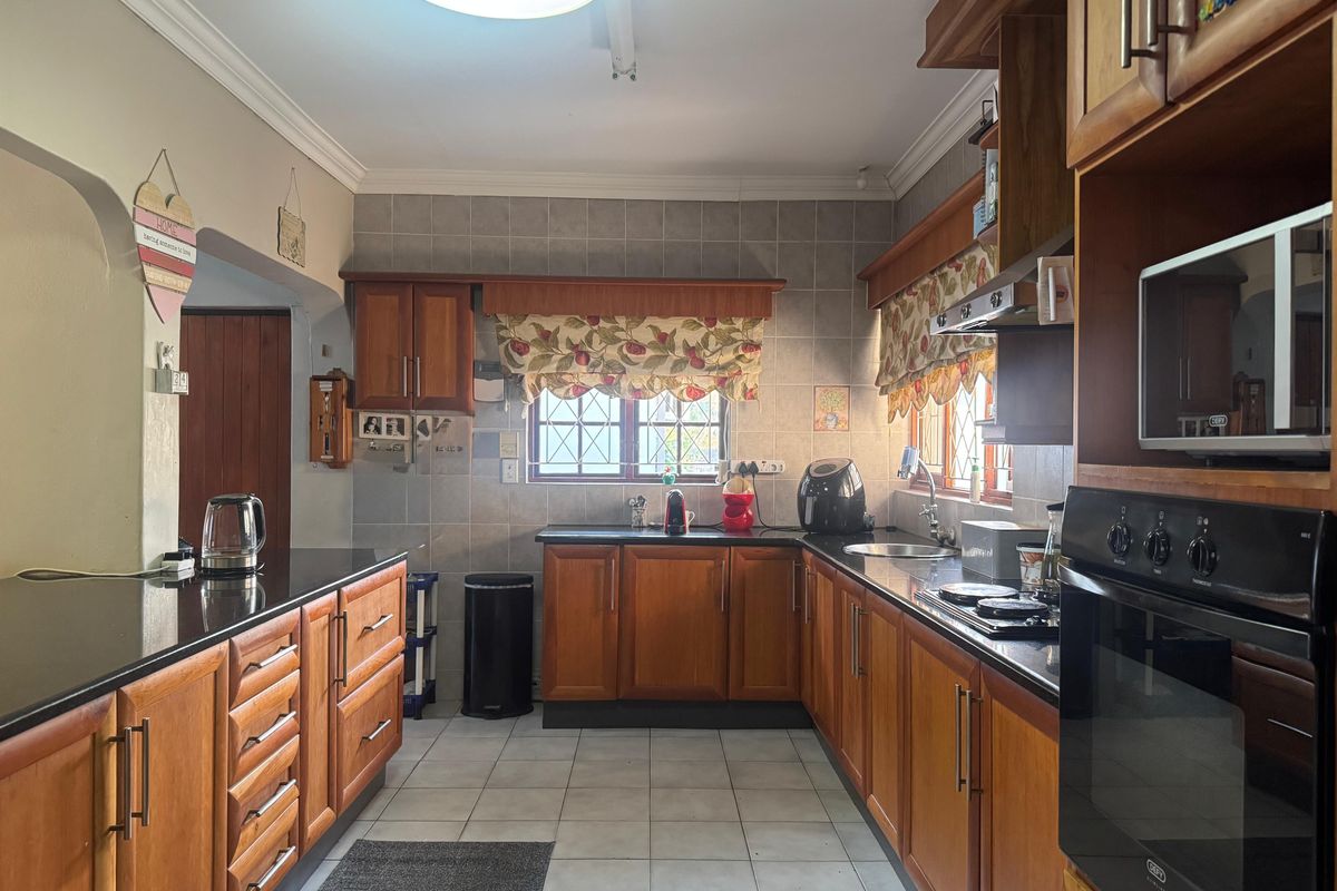 A functional kitchen featuring warm wooden cabinetry, granite countertops, built-in oven, hob, and tiled finishes, offering a classic and practical workspace.