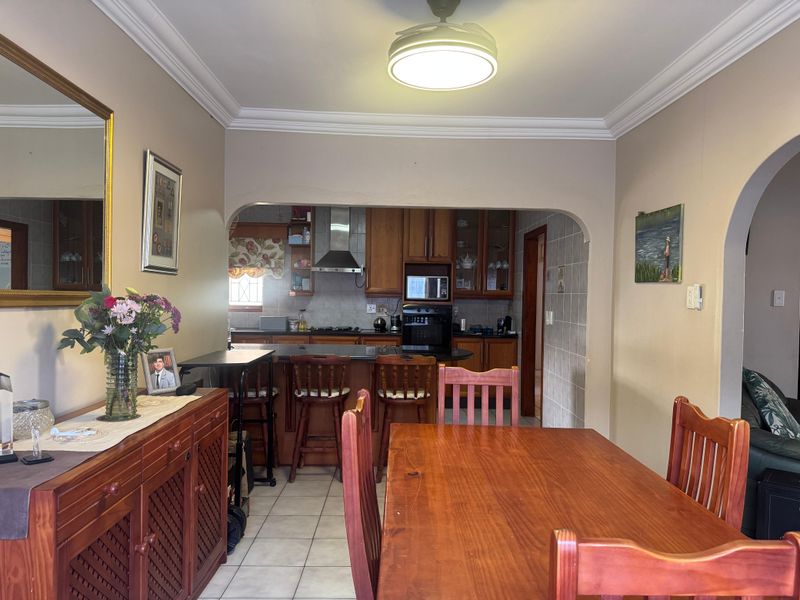 Open plan dining area leading into a functional kitchen with wooden cabinetry, built-in oven, extractor fan, and tiled flooring.