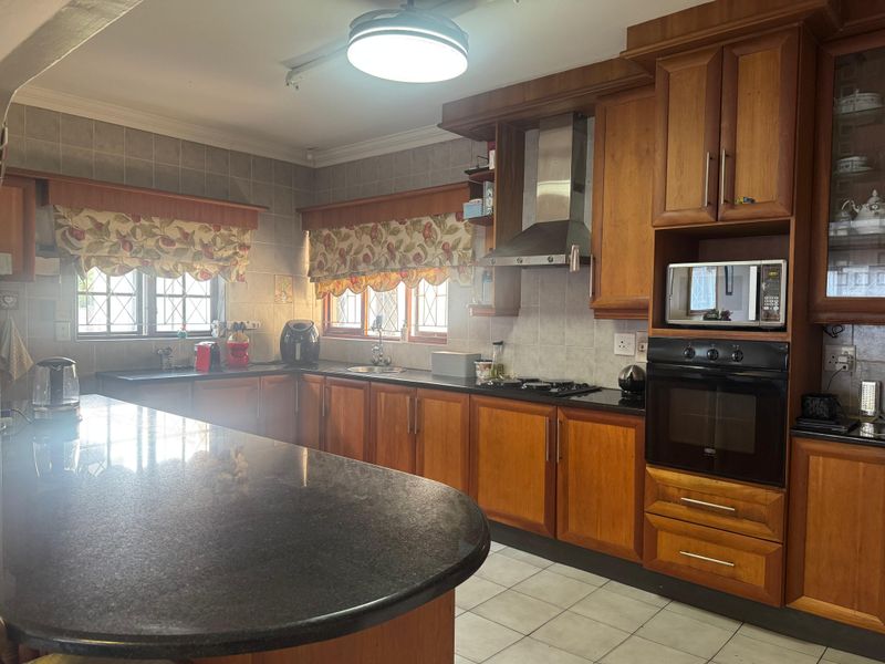 A functional kitchen featuring wooden cabinetry, granite countertops, a built-in oven, gas hob, and a breakfast bar island.