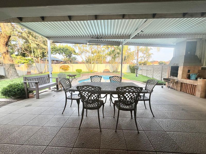 Spacious covered patio featuring a built-in braai, tiled flooring, and direct access to the swimming pool and garden area.
