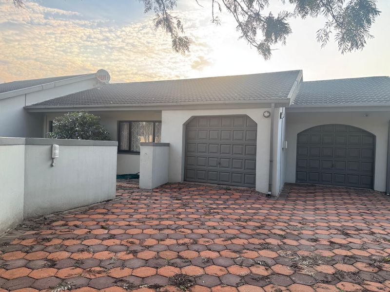 Front view of a residential property featuring a double garage, paved driveway, and secure boundary wall.
