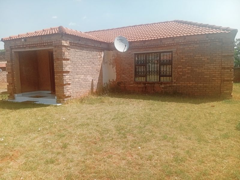 Single-story brick house featuring a tiled roof, security bars on windows, and a covered entrance area, set on a large grassed plot.