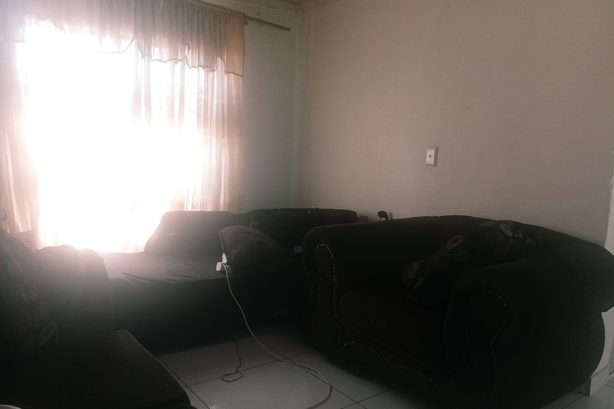 A living room area featuring tiled flooring and natural light from a large window, currently requiring cosmetic updates to improve the overall aesthetic.