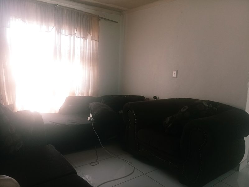 A living room area featuring tiled flooring and natural light from a large window, currently requiring cosmetic updates to improve the overall aesthetic.
