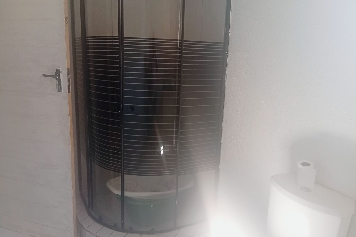 A compact bathroom featuring a curved shower enclosure and a standard toilet, requiring minor finishing touches to the door frame and paintwork.