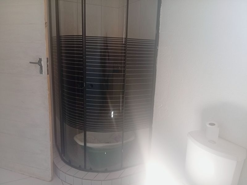 A compact bathroom featuring a curved shower enclosure and a standard toilet, requiring minor finishing touches to the door frame and paintwork.