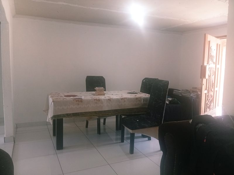 A dining area featuring white tiled flooring and a wooden door, currently requiring ceiling finishing and improved lighting to enhance the space.