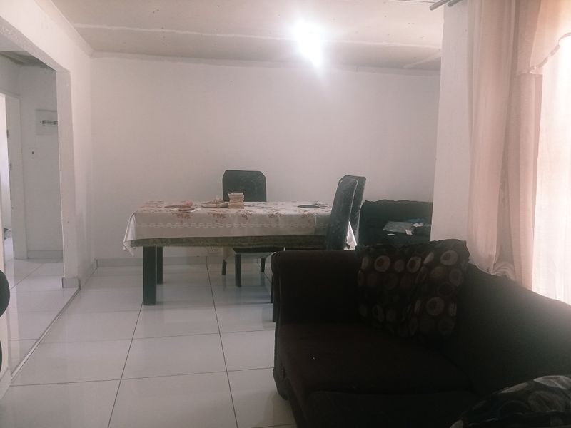 Open plan living and dining area featuring white tiled flooring and plain walls, requiring cosmetic updates to improve the overall aesthetic.