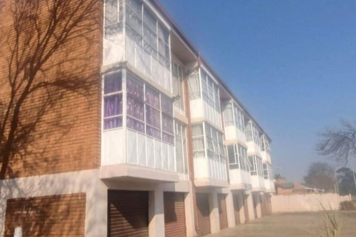 Rear view of a multi-story townhouse complex featuring face brick construction, enclosed balconies, and ground-level garages with roller shutter doors.