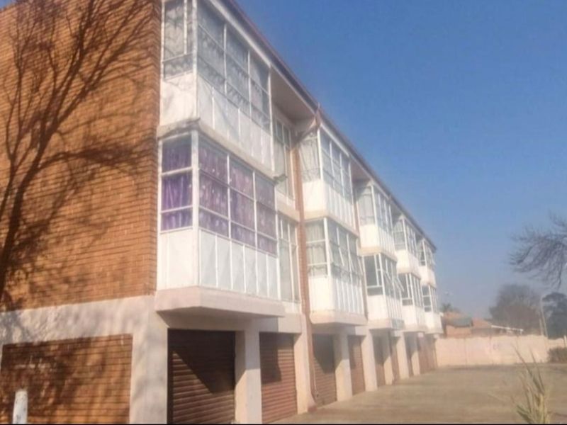 Rear view of a multi-story townhouse complex featuring face brick construction, enclosed balconies, and ground-level garages with roller shutter doors.