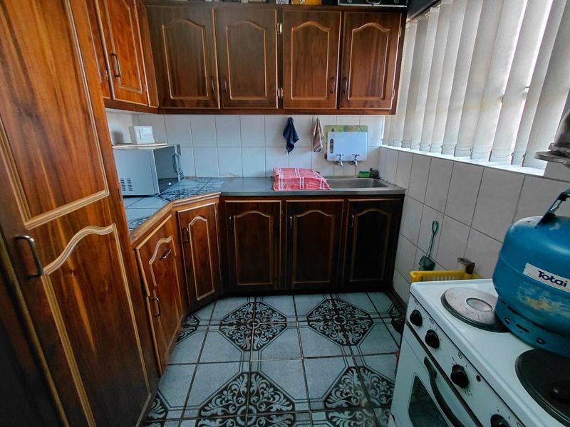 A compact kitchen featuring traditional wooden cabinetry, stainless steel sink, tiled backsplash, and patterned floor tiles, offering a functional layout with gas cooking facilities.
