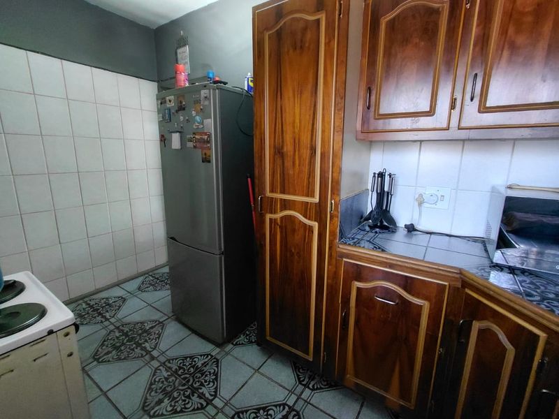 A functional kitchen featuring traditional wooden cabinetry, tiled backsplash, and patterned floor tiles, offering potential for a modern renovation.