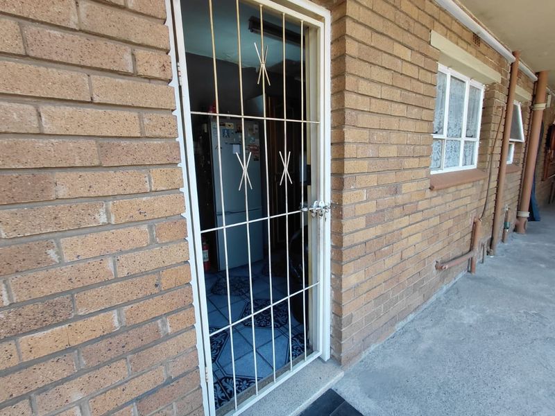Exterior view of a townhouse entrance featuring a brick facade, concrete walkway, and a secure metal security gate.