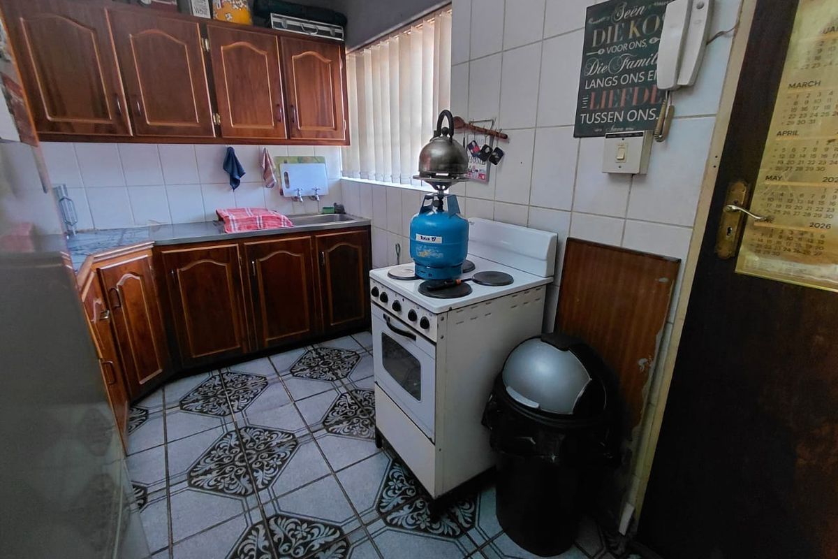 A dated kitchen featuring wooden cabinetry, tiled flooring, and a freestanding stove, offering potential for a modern renovation.
