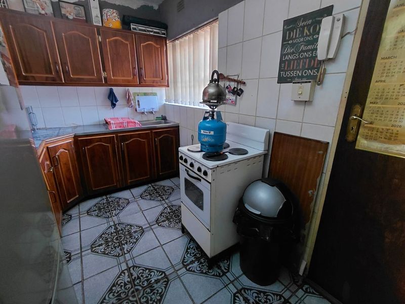 A dated kitchen featuring wooden cabinetry, tiled flooring, and a freestanding stove, offering potential for a modern renovation.