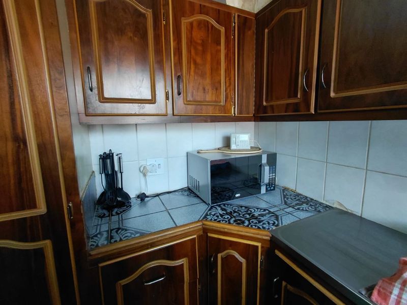 A compact kitchen featuring traditional wooden cabinetry, tiled countertops, and a tiled backsplash, offering a dated aesthetic ready for modernization.